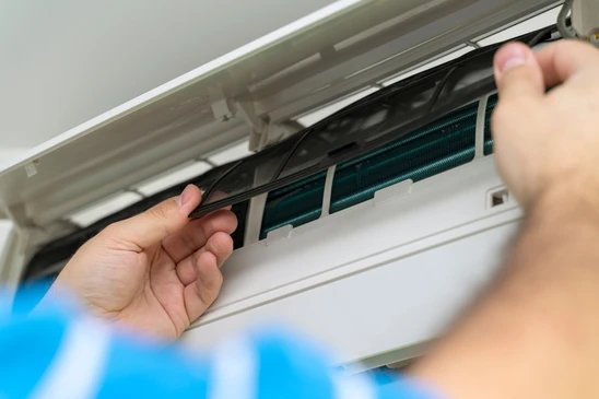 Personne effectuant la maintenance d'un climatiseur mural intérieur, manipulant le filtre à air avec les deux mains