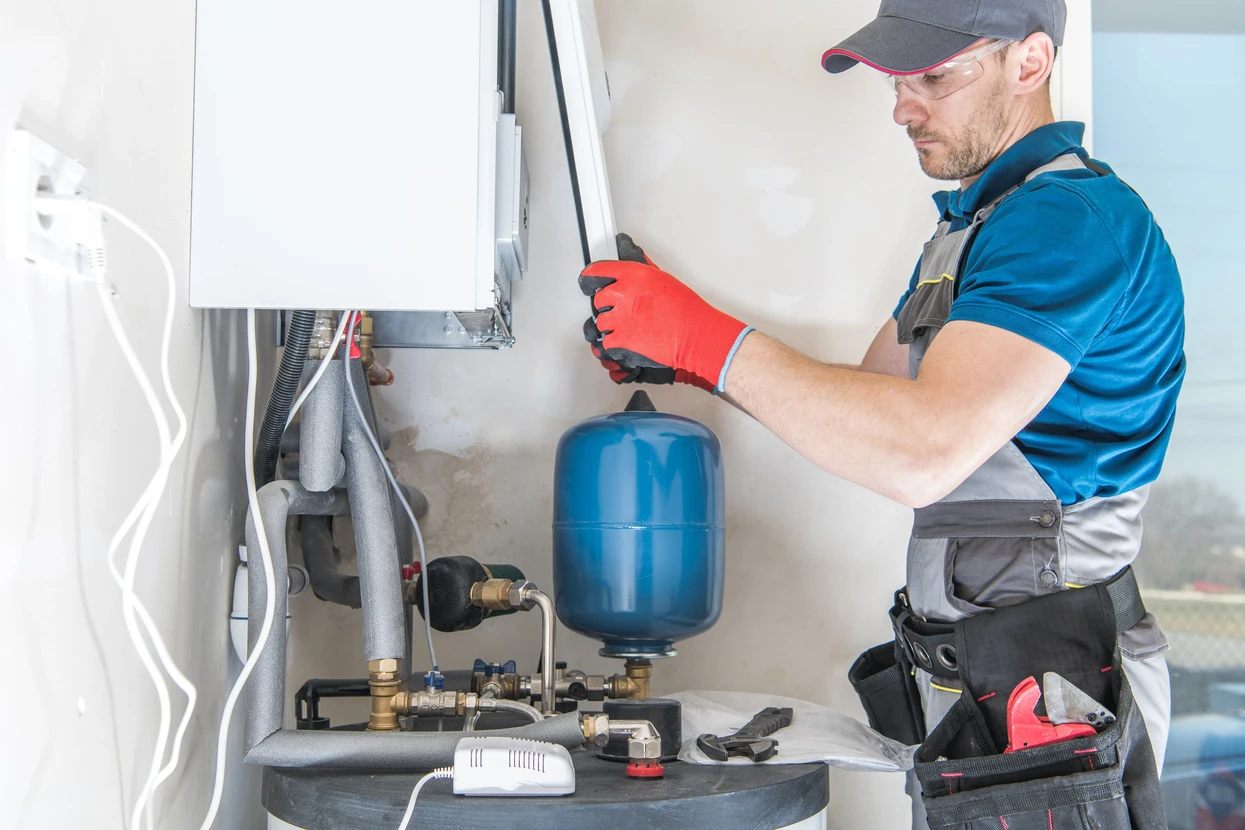 Technicien en plomberie intervenant sur installation de chauffage domestique dans local technique résidentiel