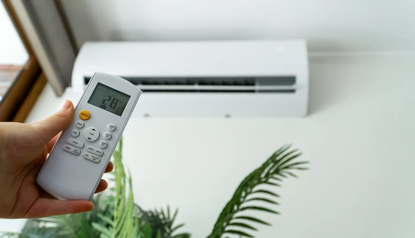 Intérieur moderne avec système de climatisation split composé d'une unité extérieure compacte blanche avec ventilateur bleu et grilles d'aération, unité intérieure murale avec affichage digital et évacuation d'air, télécommande avec écran LCD affichant 24°C