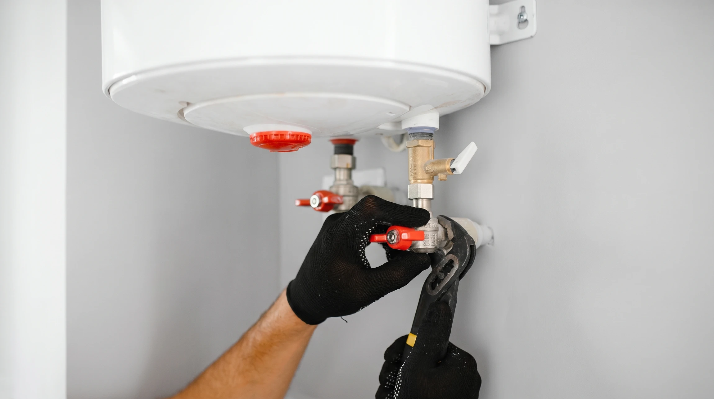 Technicien en salopette bleue effectuant la maintenance d'une chaudière murale dans un intérieur domestique moderne