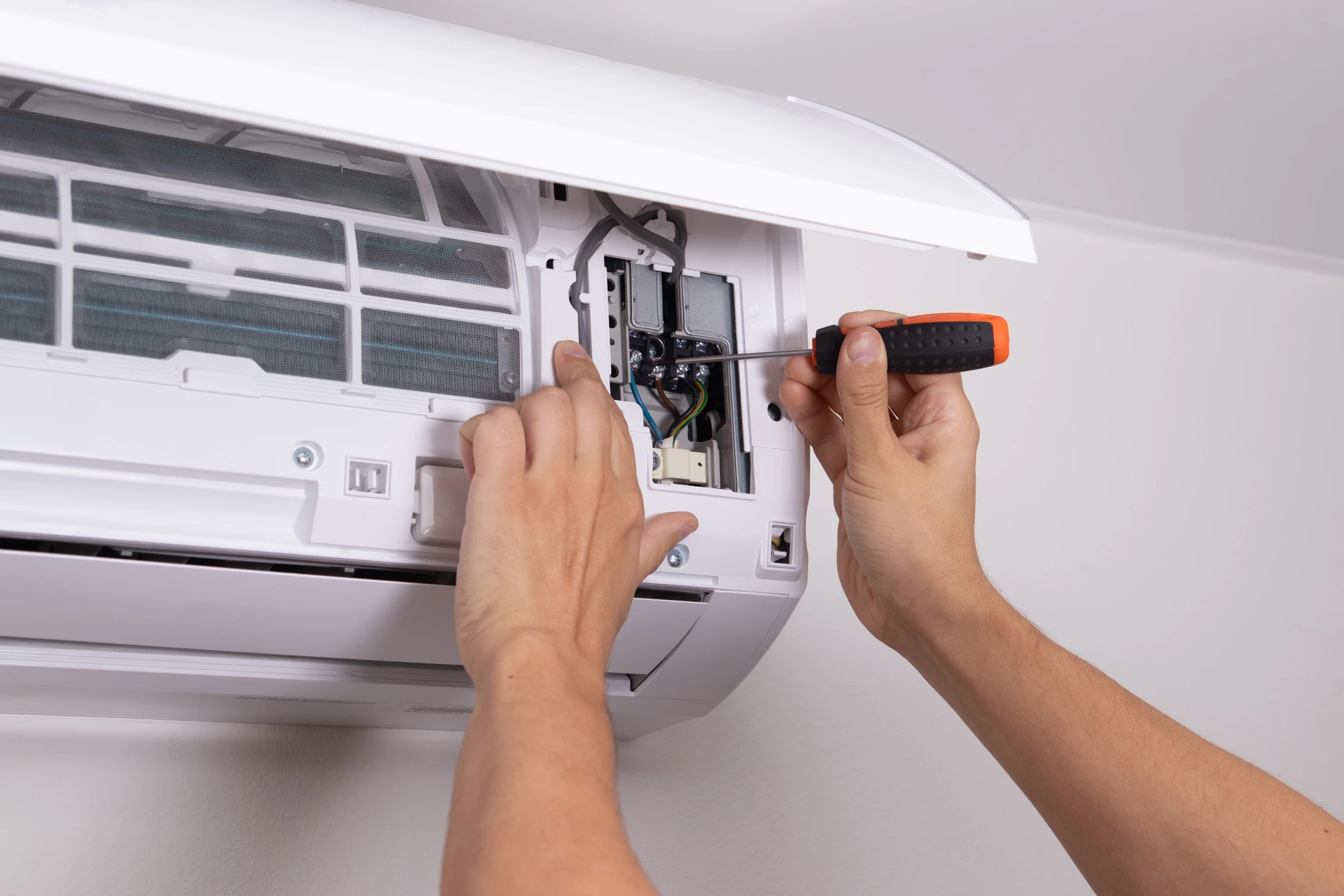 Technicien en combinaison de travail effectuant la maintenance d'une unité de climatisation murale dans un environnement intérieur